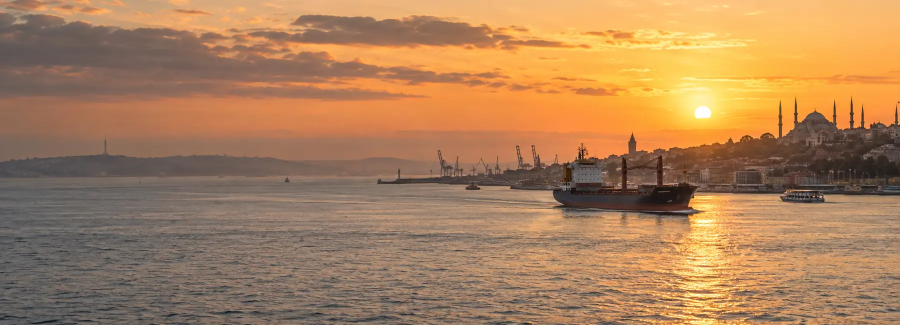 Illustrative cargo vessel and Istanbul-inspired waterfront at sunset